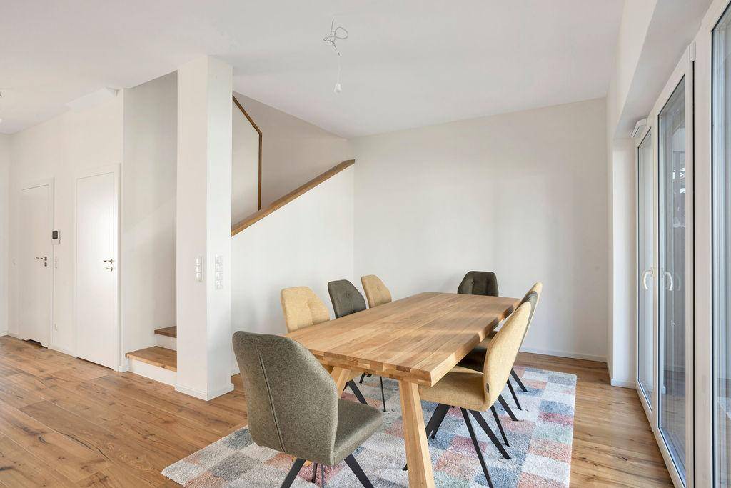 Heller Essbereich mit großem Holztisch und modernen Stühlen, angrenzend an eine Holztreppe.