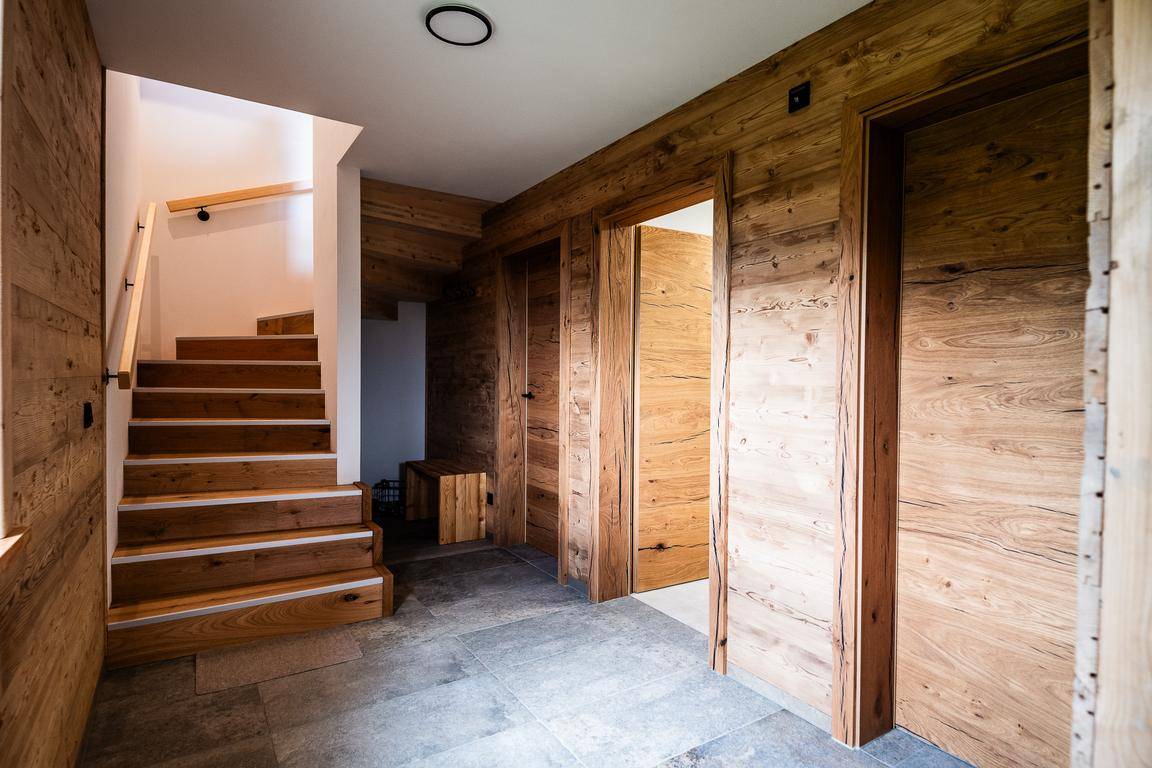 Heller Flur mit Holzwänden, Holztüren und einer Holztreppe, die in die obere Etage führt.