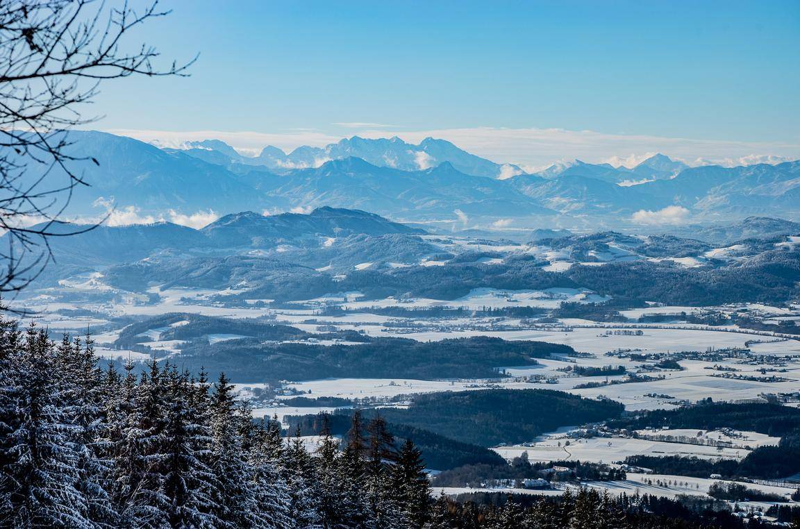 Weitläufiger Panoramablick über eine verschneite Berglandschaft und ein winterliches Tal.