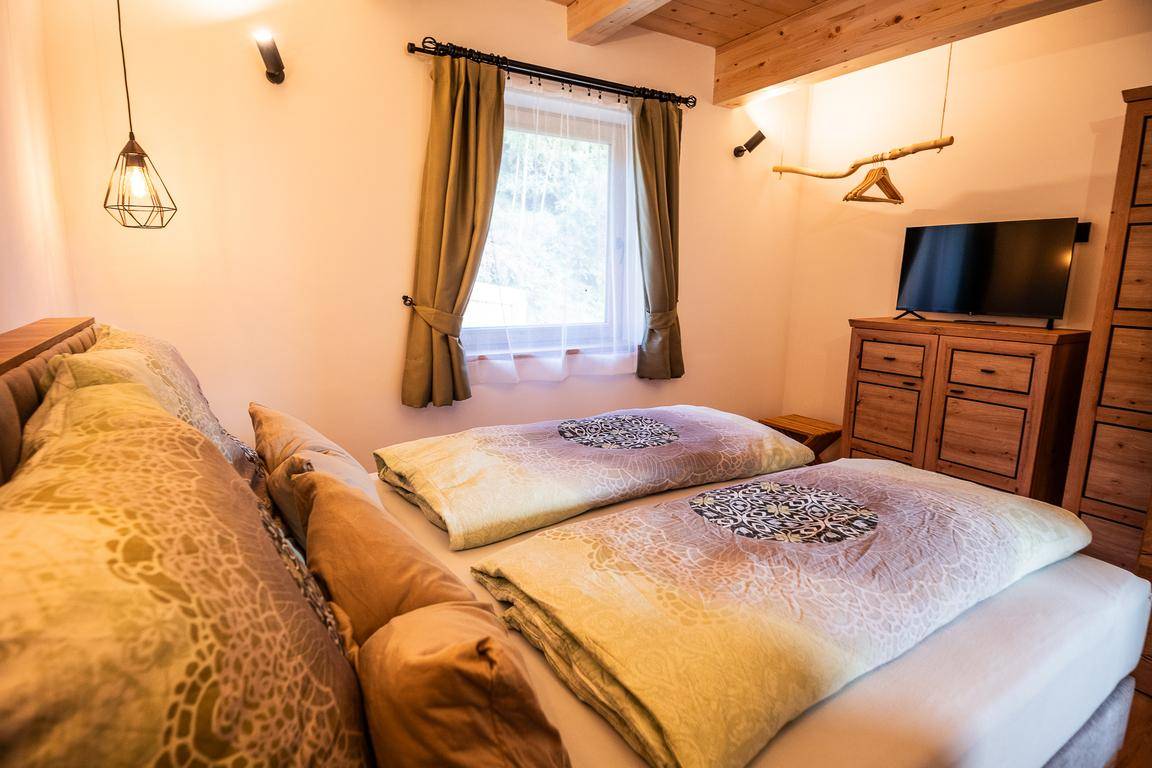 Gemütliches Schlafzimmer mit Doppelbett, Holzmöbeln und einem Fenster mit Blick ins Grüne.