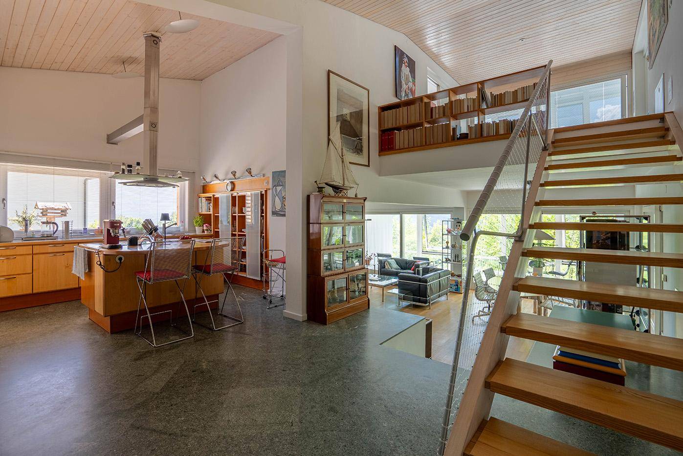 Offener Wohnbereich mit Küche, Essbereich und Treppe zu einer Galerie, mit Blick ins Grüne.