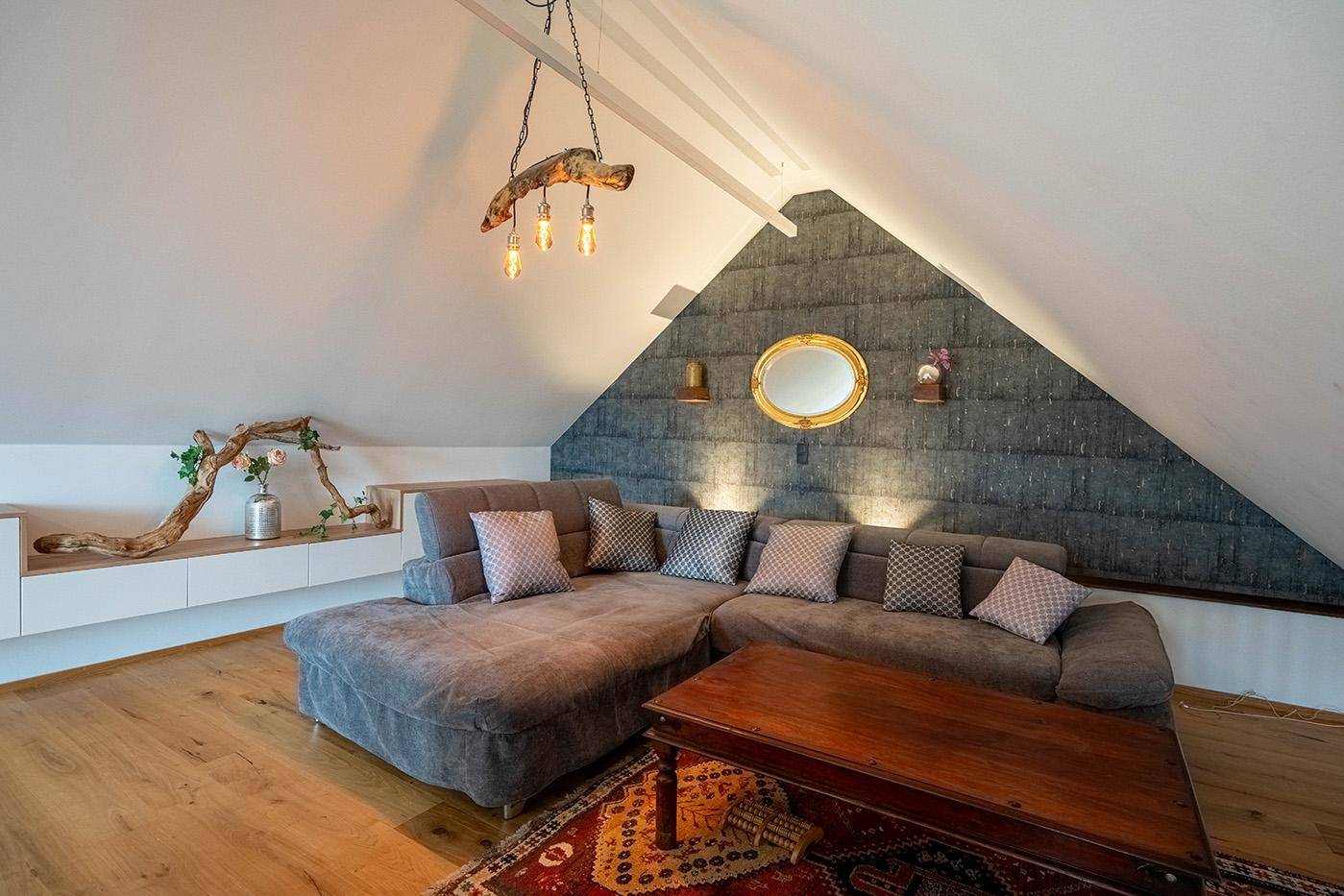 Helles Wohnzimmer im Dachgeschoss mit großem Ecksofa und Holzboden.