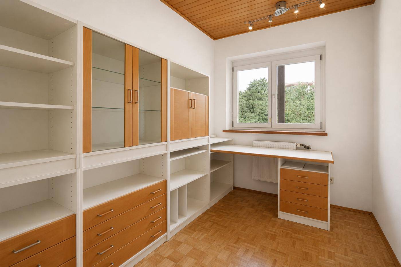 Helles Arbeitszimmer mit Einbauregalen, Schreibtisch, Parkettboden und Fenster mit Ausblick.