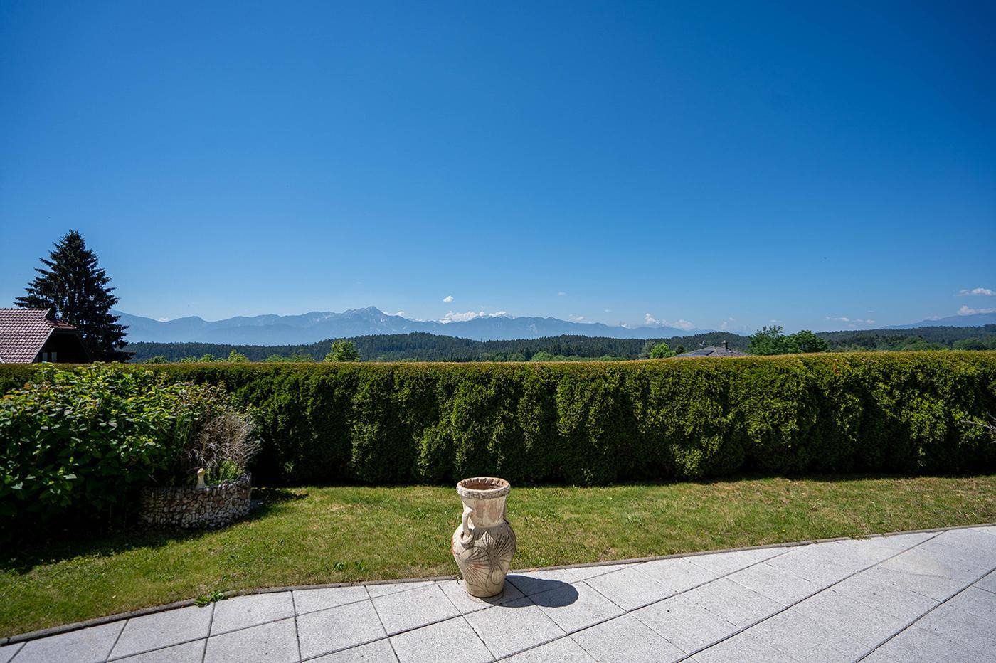 Gepflegter Gartenbereich mit hoher Hecke und weitem Blick auf die umliegende Berglandschaft.