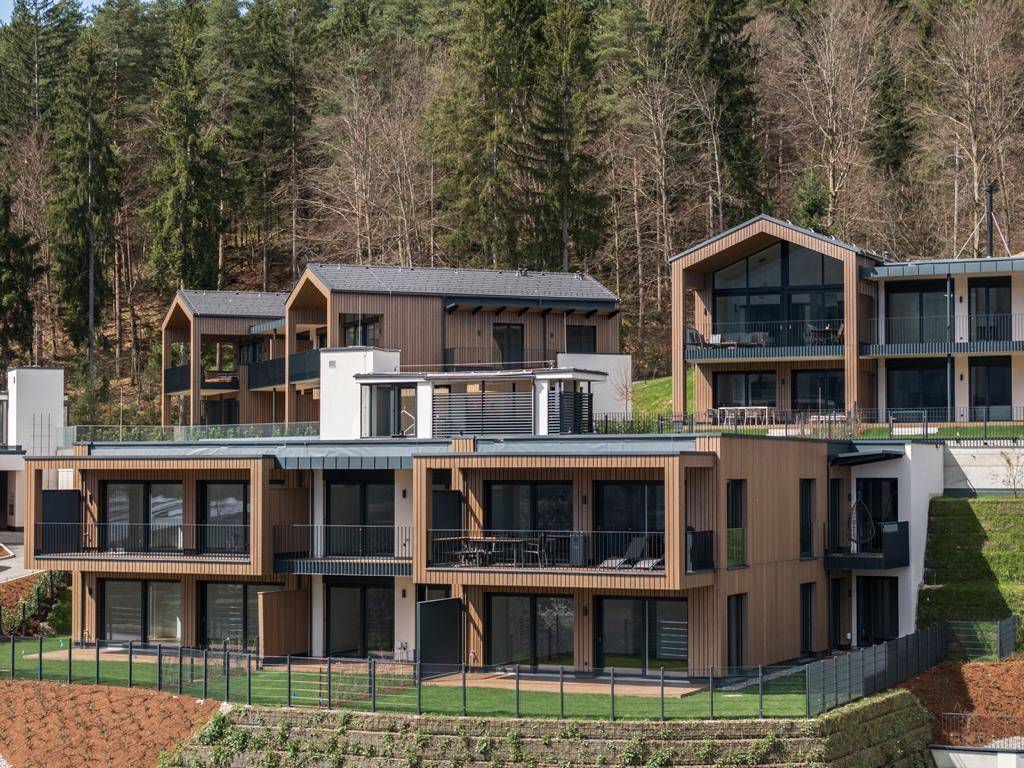 Moderne Wohngebäude mit Holzfassaden und großen Balkonen, eingebettet in eine bewaldete Hanglage.