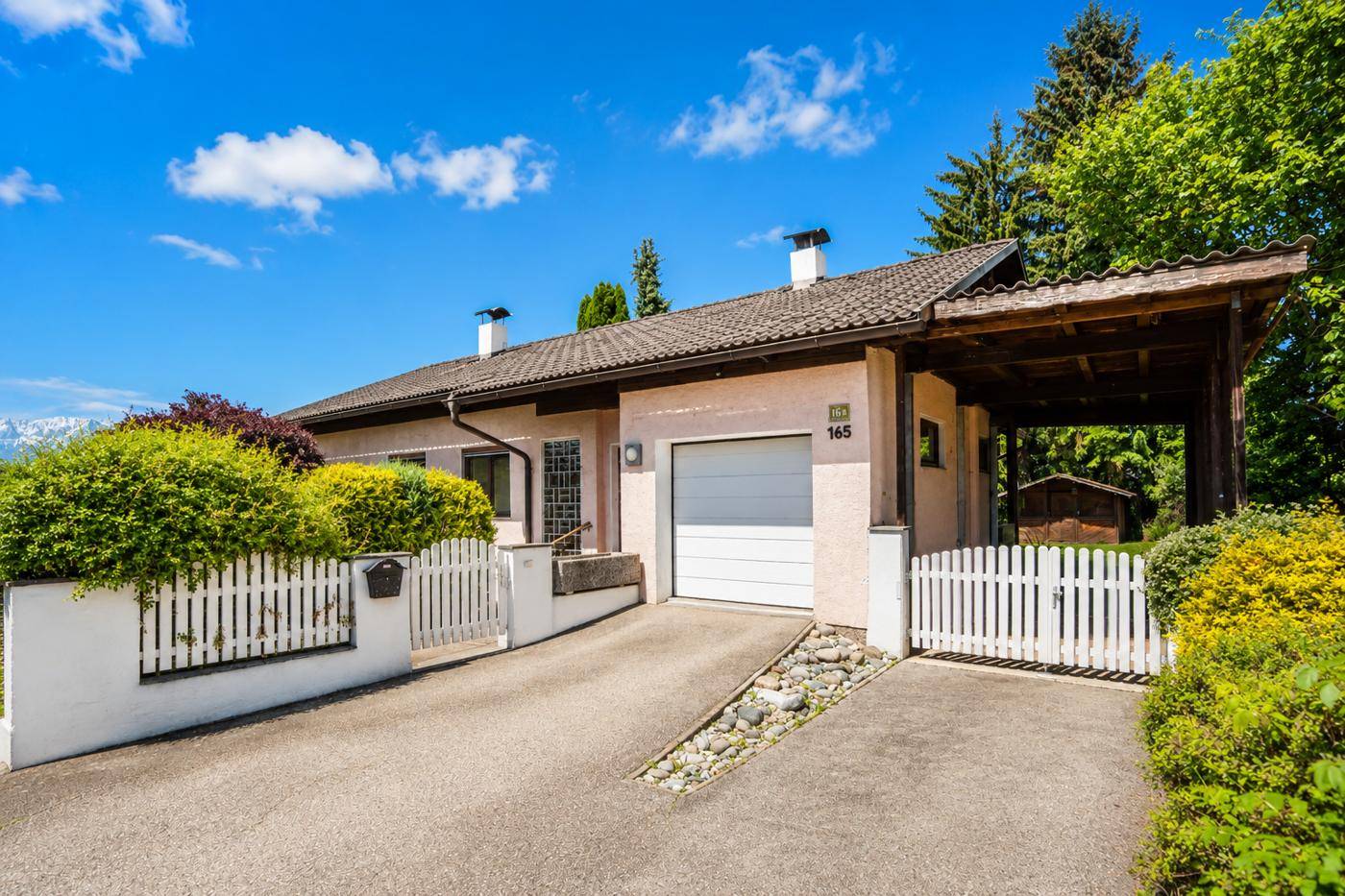 Vorderansicht eines Einfamilienhauses mit Garage, Carport und weißem Lattenzaun.