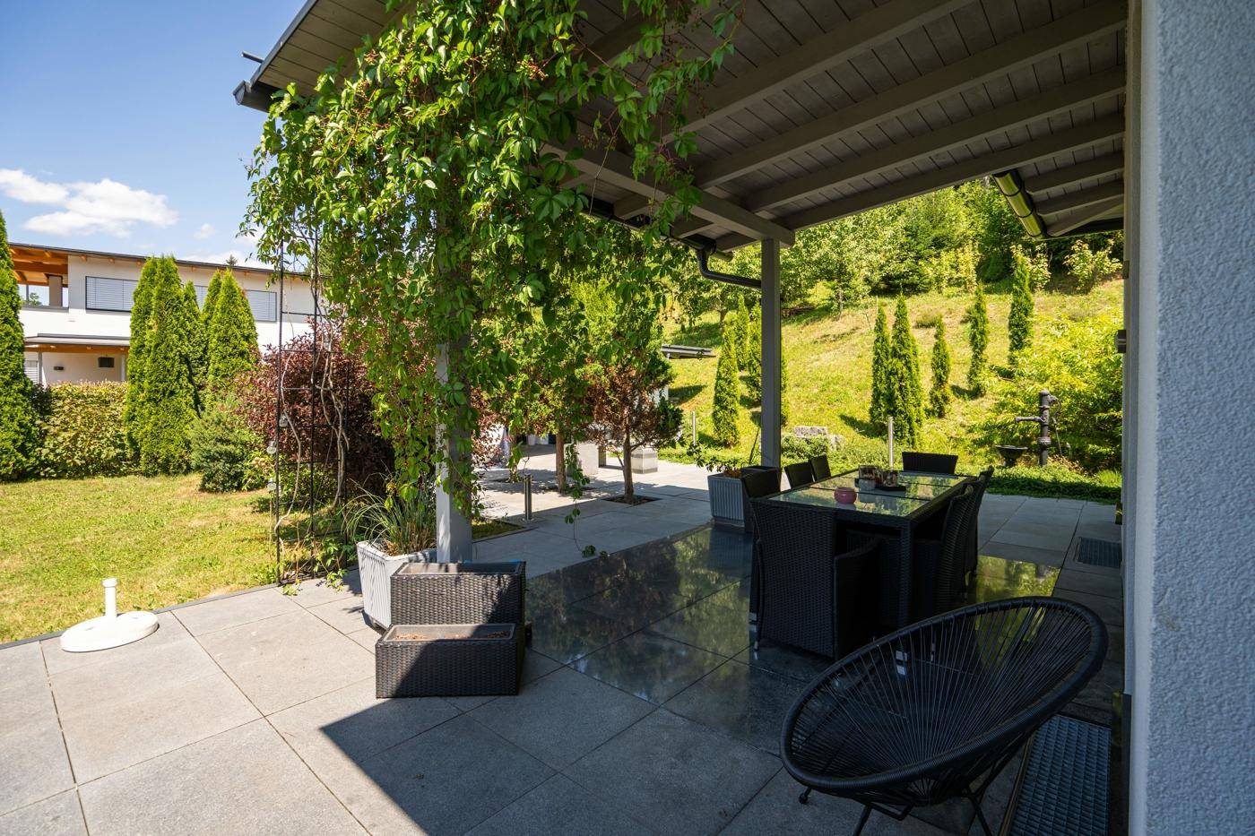 Überdachte Terrasse mit Sitzgelegenheiten und Blick auf den grünen Garten und die Hügellandschaft.