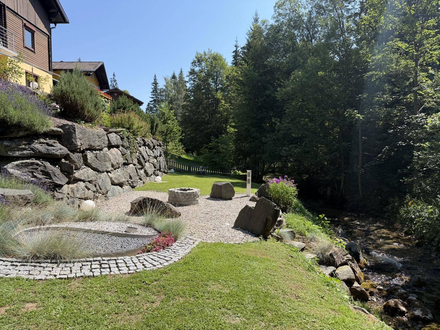 Idyllischer Gartenbereich mit Feuerstelle, Kiesfläche und direktem Zugang zum Bachlauf.