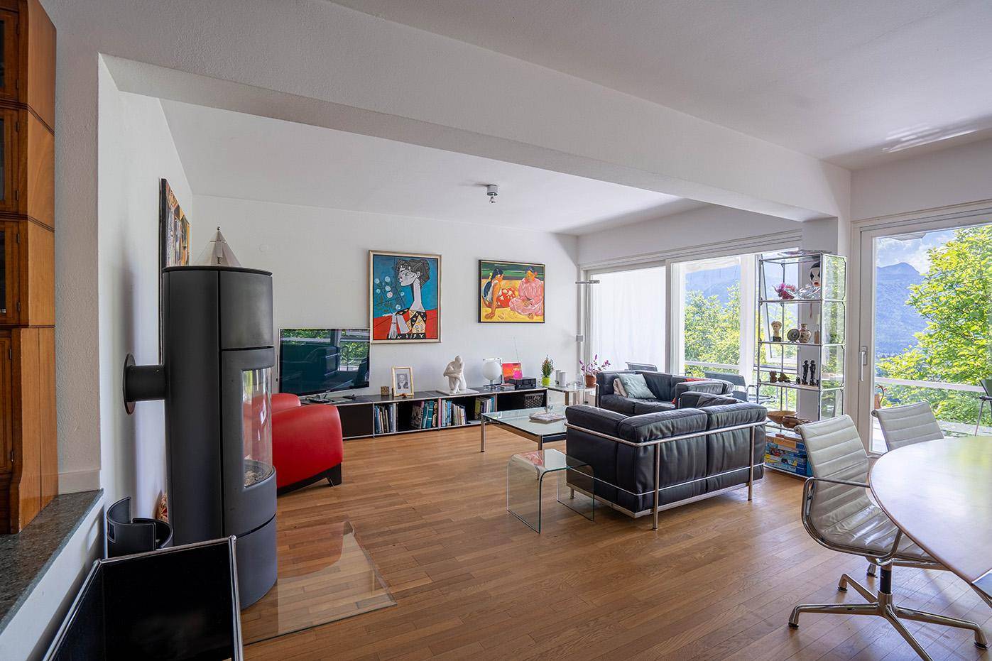 Helles Wohnzimmer mit Holzboden, Kaminofen und weitem Bergblick durch große Fenster.
