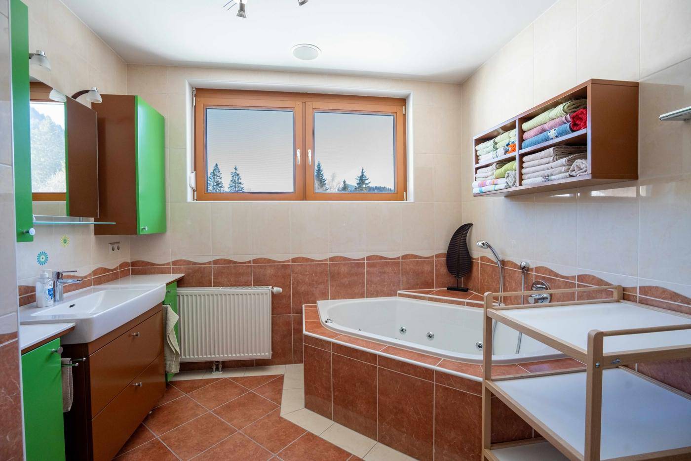 Geräumiges Badezimmer mit Eckbadewanne, Fliesen und farbigen Schränken.