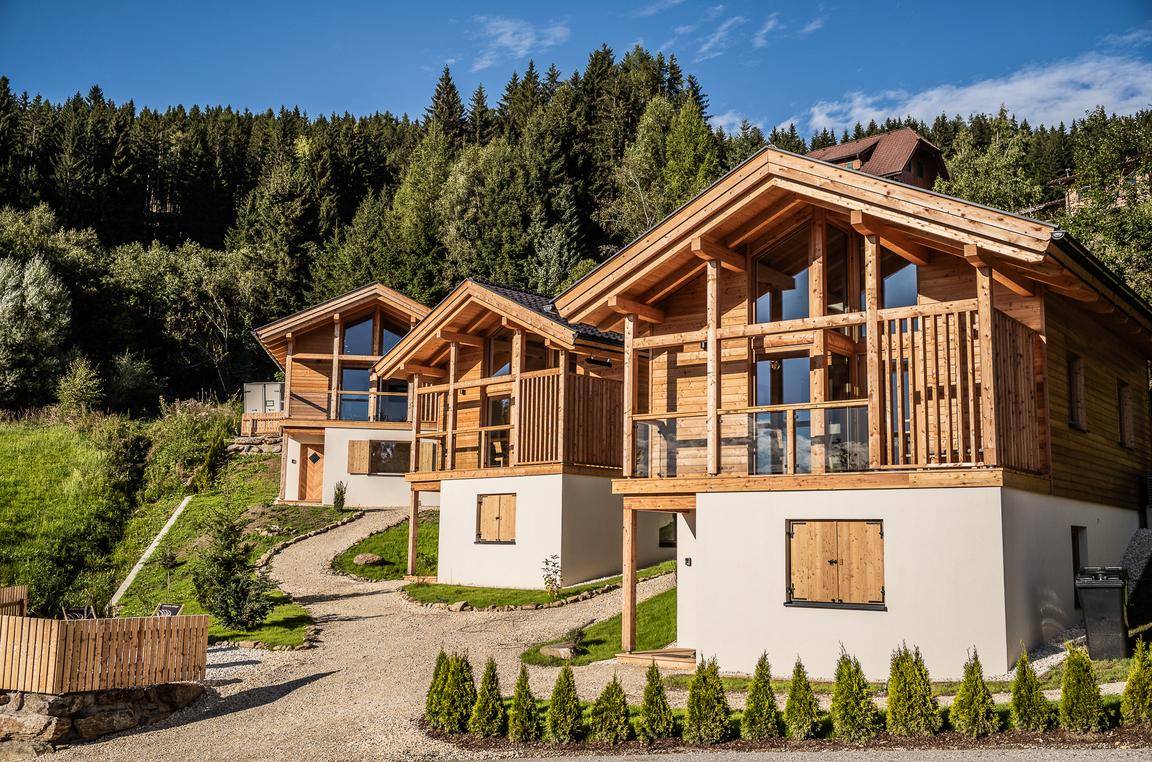 Moderne Holzchalets mit großen Fenstern und Balkonen, eingebettet in eine grüne Hügellandschaft.