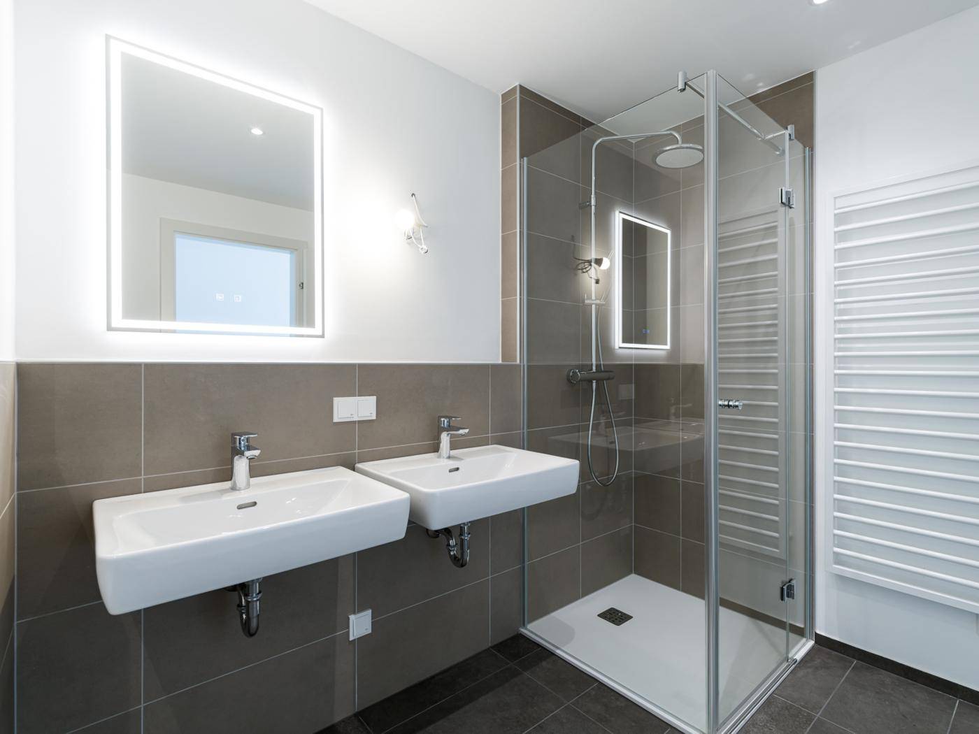 Modernes Badezimmer mit Doppelwaschbecken, großer begehbarer Dusche und beheiztem Handtuchhalter.
