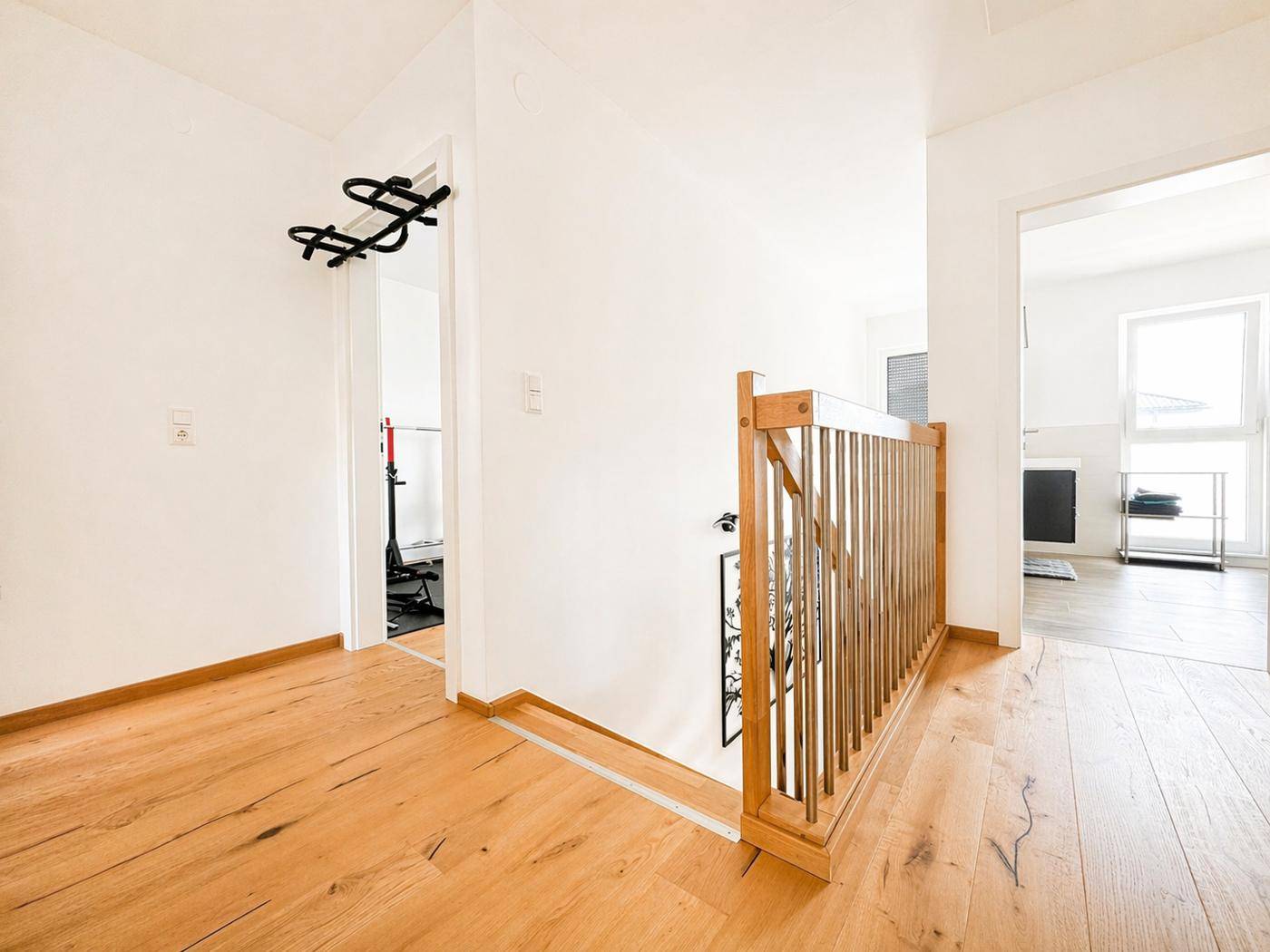 Heller Flur im Obergeschoss mit Holzgeländer und durchgehendem Parkettboden.