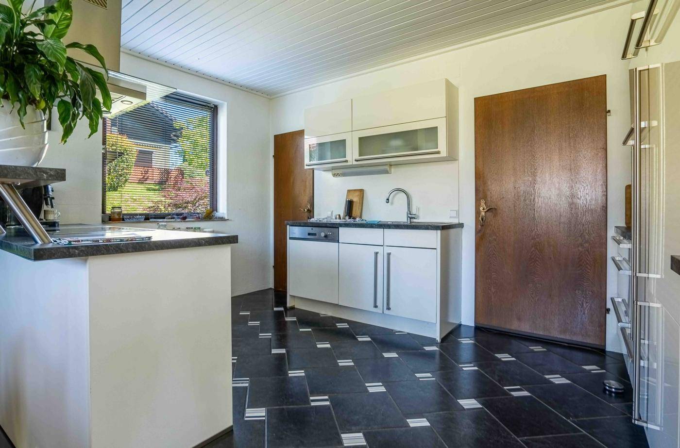Funktionale Küche mit weißen Schränken, dunklem Fliesenboden und Fenster.