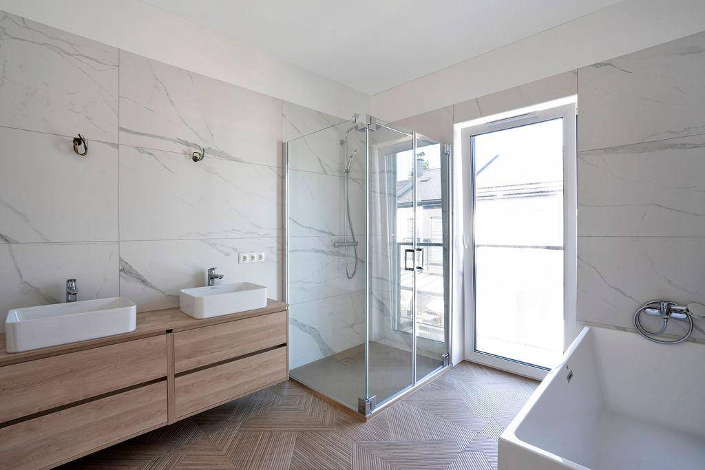 Modernes Badezimmer mit Doppelwaschbecken, begehbarer Dusche, Badewanne und Fenster für Tageslicht.