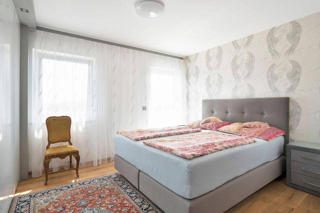 Helles Schlafzimmer mit Doppelbett, Holzboden und dekorativer Tapete an einer Wand.