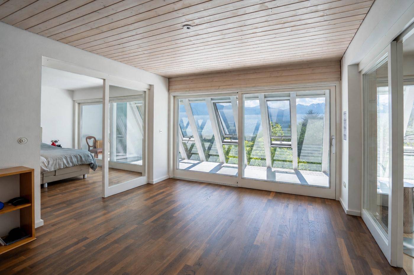 Heller Schlafbereich mit Holzboden und großen Fenstern, die einen weiten Blick bieten.