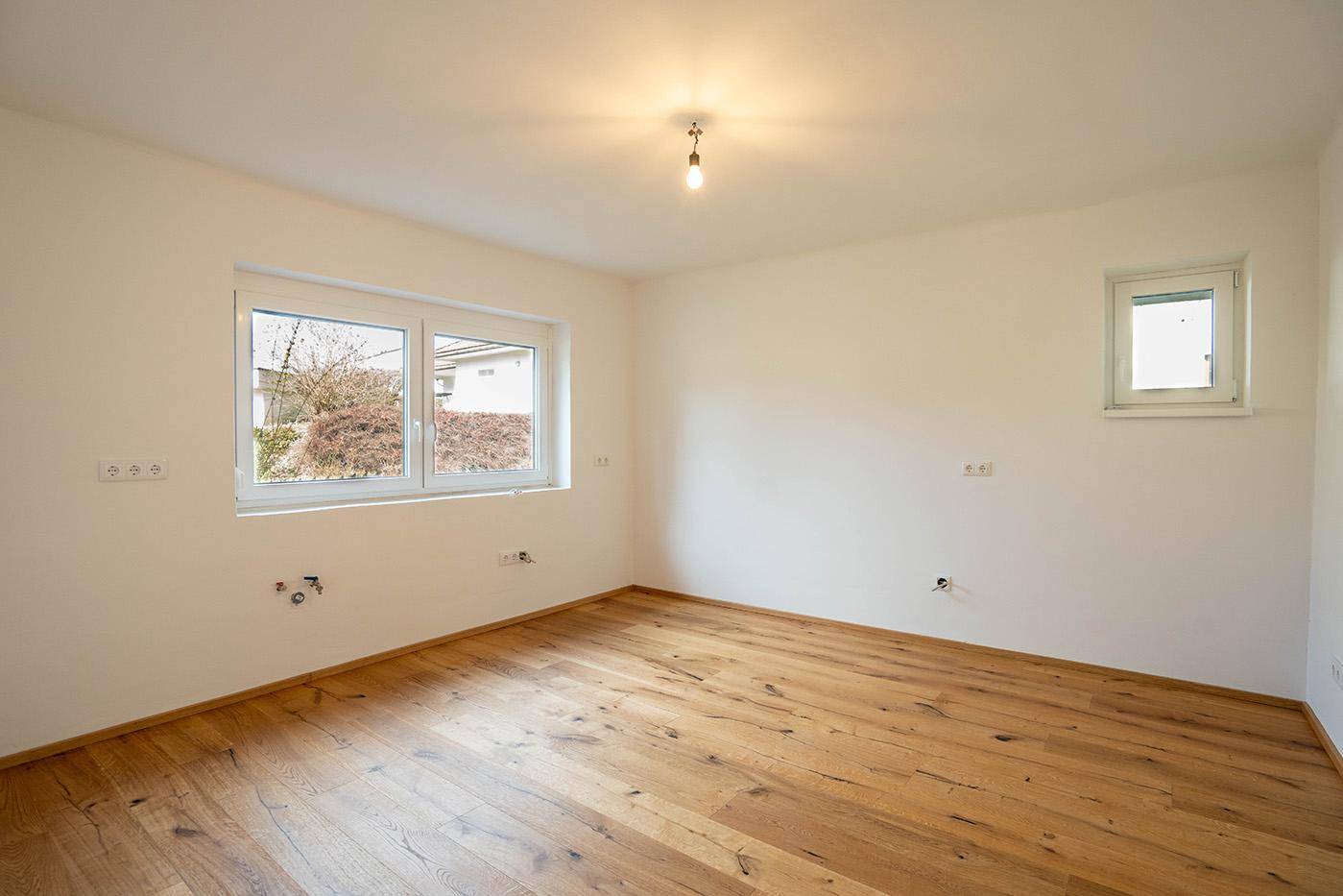 Lichtdurchfluteter, unmöblierter Raum mit zwei Fenstern und elegantem Holzfußboden.
