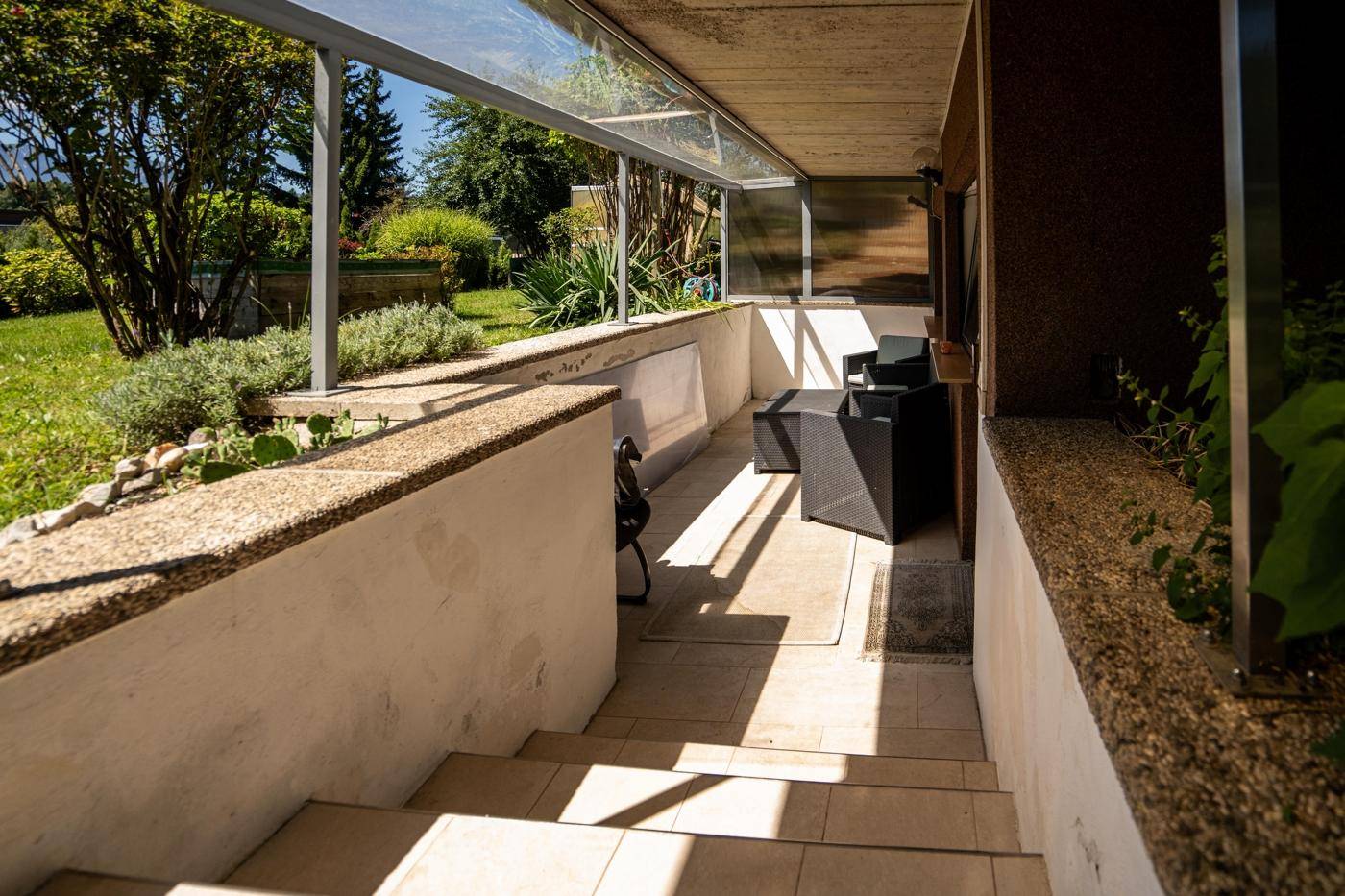 Überdachter Terrassenbereich mit Sitzgelegenheiten und Zugang zum Garten.