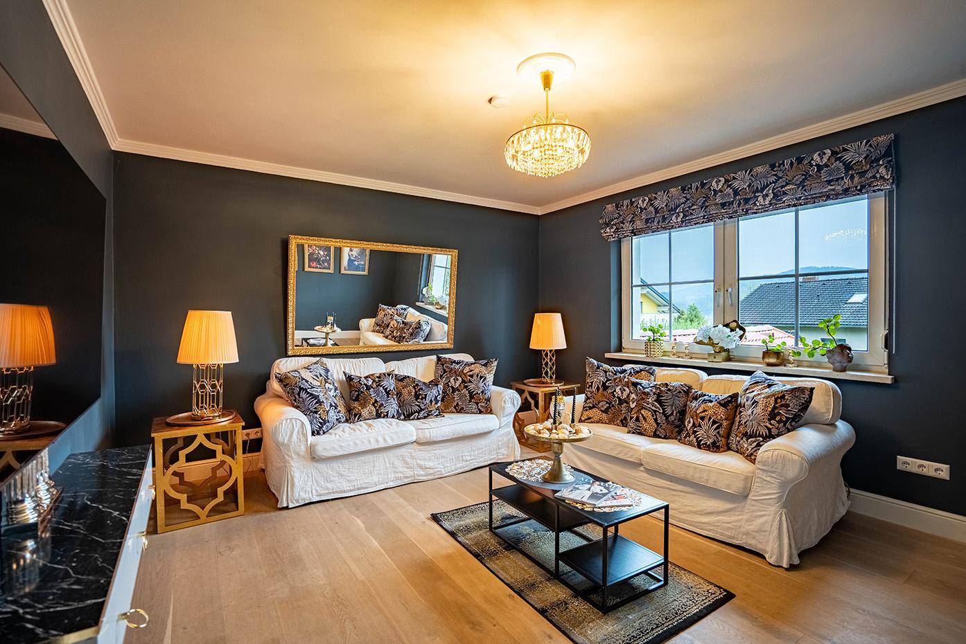 Gemütliches Wohnzimmer mit dunklen Wänden, hellen Sofas und eleganten Goldakzenten.