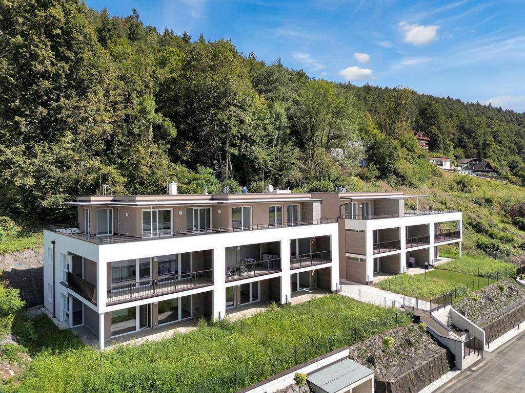 Zeitgenössische Wohngebäude in Hanglage, harmonisch in die bewaldete Umgebung integriert, mit großzügigen Balkonen.