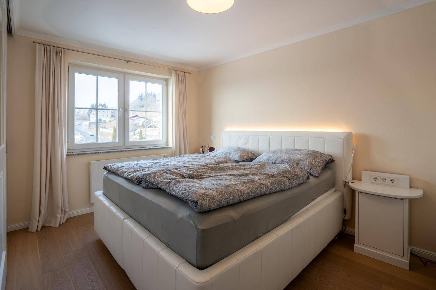 Gemütliches Schlafzimmer mit Doppelbett, Holzboden und Fenster mit Blick ins Grüne.