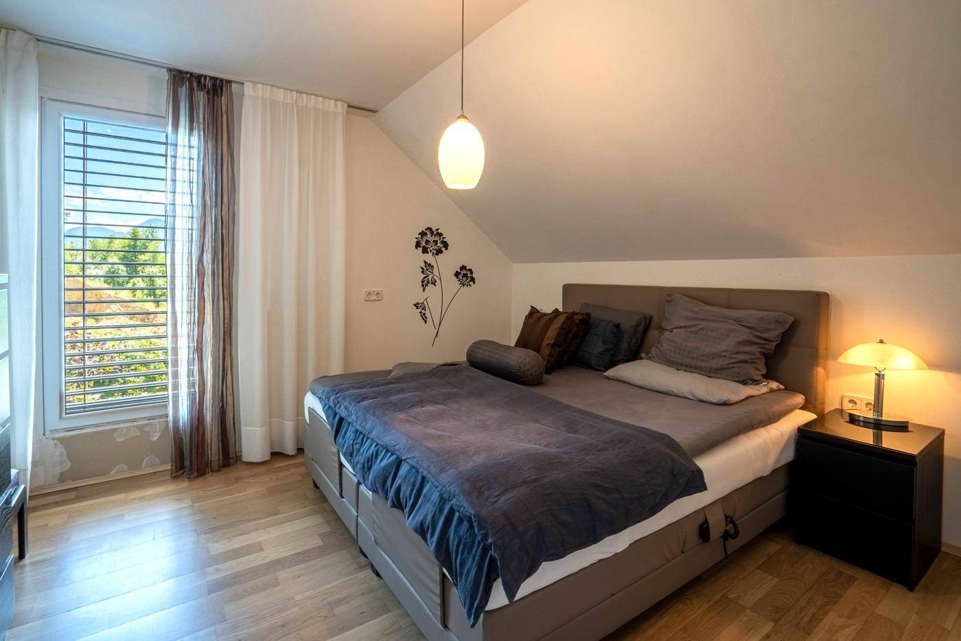 Helles Schlafzimmer im Dachgeschoss mit Holzboden, schrägen Wänden und Bergblick.