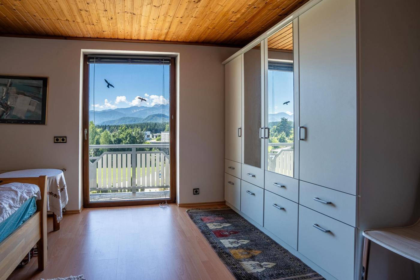 Schlafzimmer mit Holzbalkendecke, Kleiderschrank und Balkonzugang mit Bergblick.