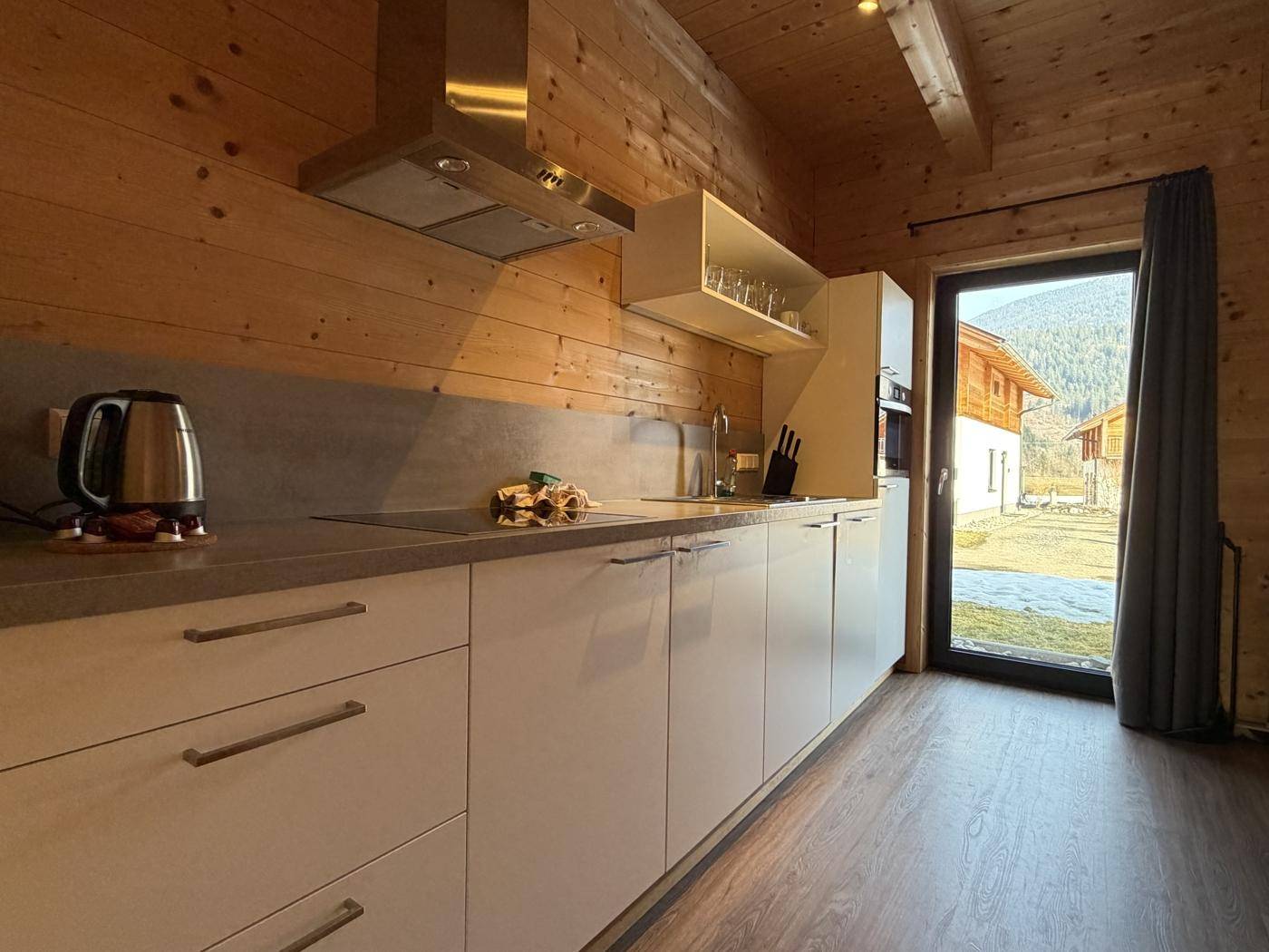 Moderne Küche mit weißen Schränken, Holzvertäfelung und Blick ins Grüne.