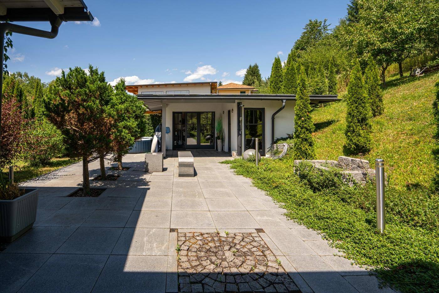 Gepflasterter Weg entlang des Hauses mit gepflegtem Garten und grüner Bepflanzung.