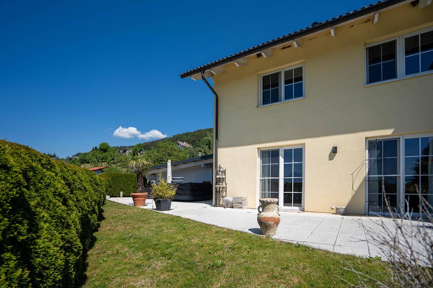 Seitlicher Blick auf das Haus mit gepflasterter Terrasse und grüner Hecke im Garten.