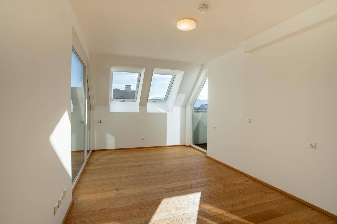 Leeres Schlafzimmer mit Holzboden, Dachfenstern und Zugang zu einem Außenbereich.