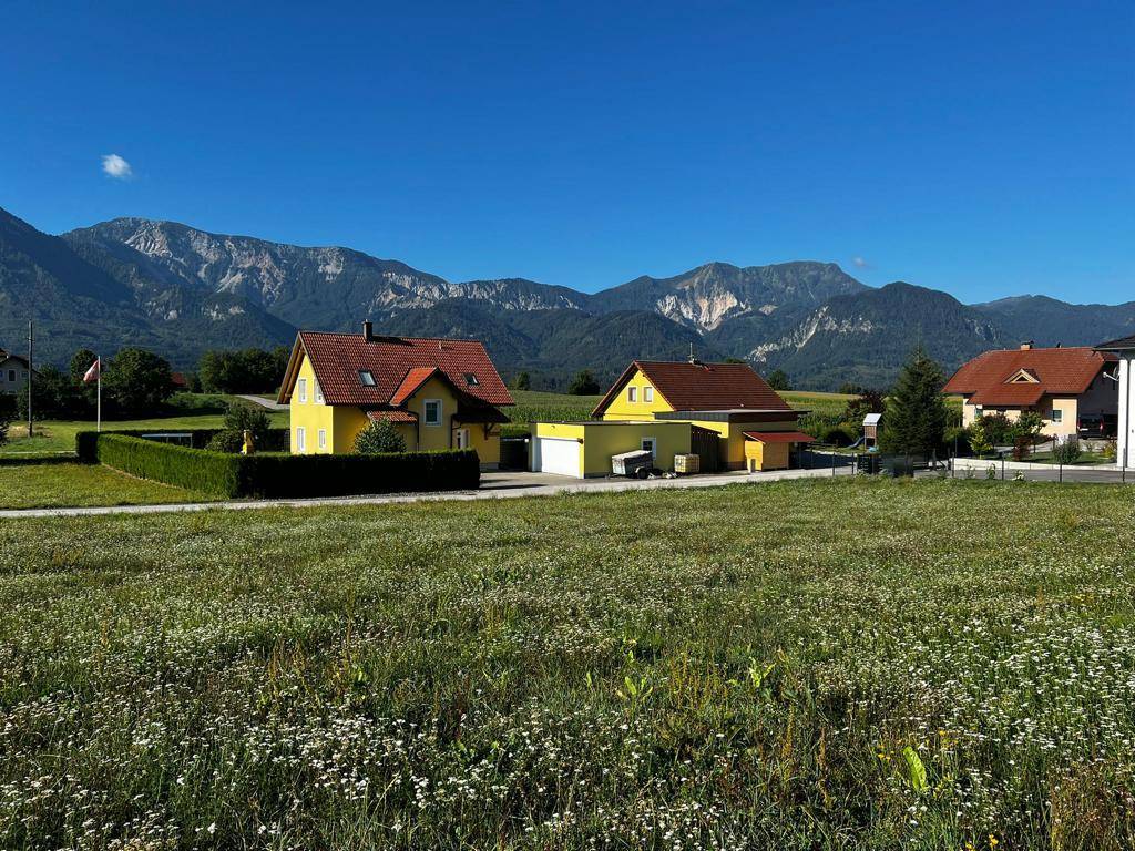 Zwei gelbe Häuser mit roten Dächern in einer idyllischen Landschaft mit majestätischem Bergblick.