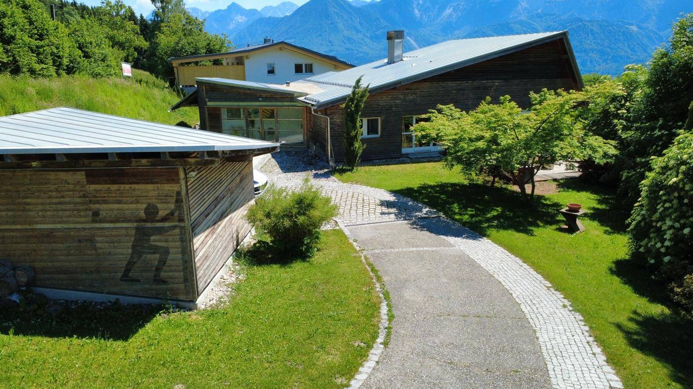 Zufahrt zum modernen Haus mit Holzfassade und Blick auf die umliegende Berglandschaft.