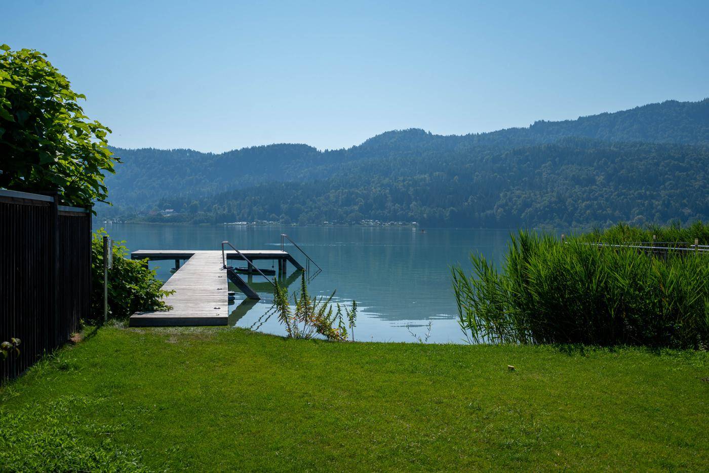 Gepflegte Rasenfläche mit direktem Zugang zu einem Holzsteg am Seeufer und Bergblick.