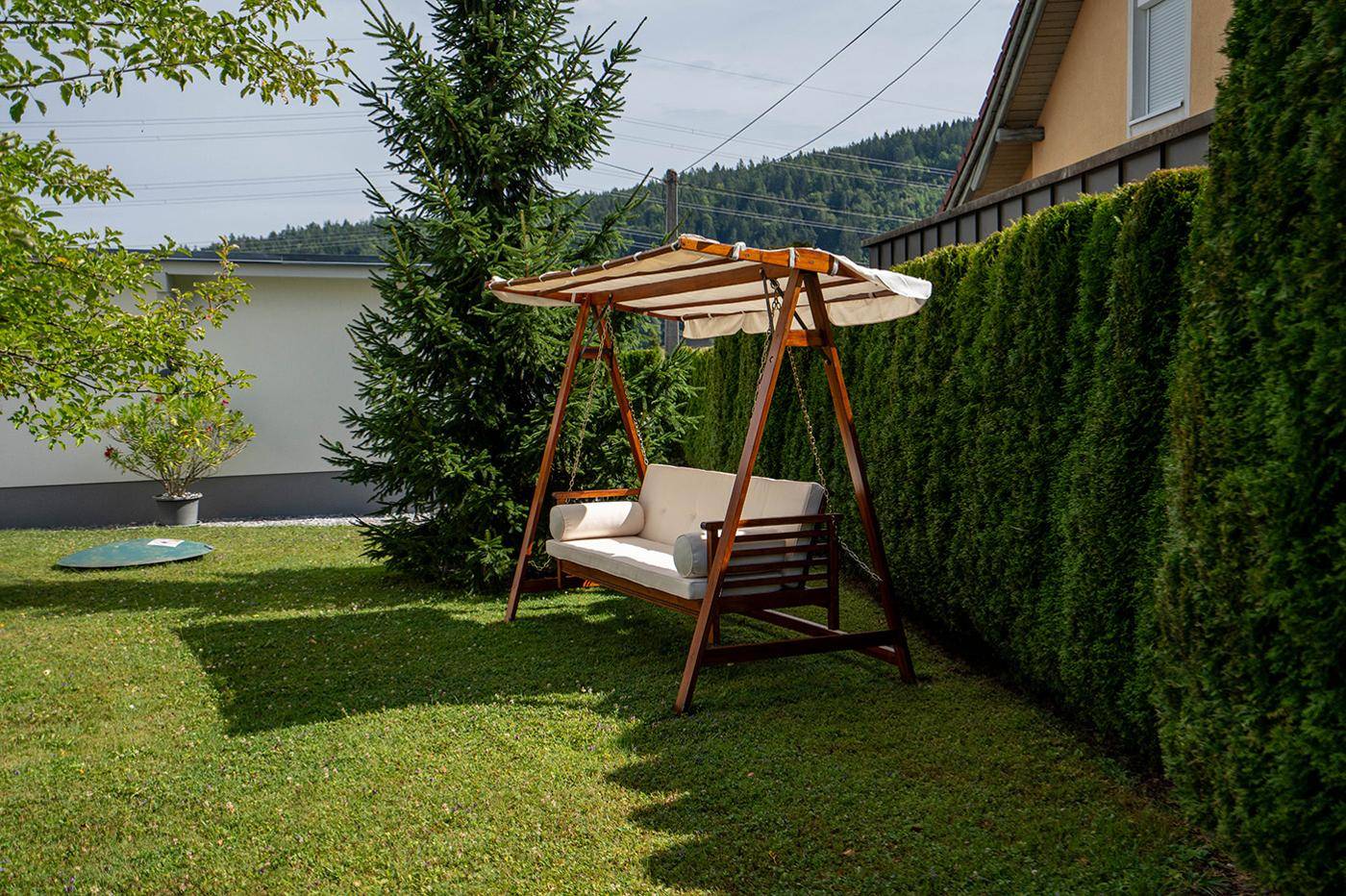 Grüner Garten mit einer Holzschaukel und einer hohen Hecke, die Privatsphäre bietet.