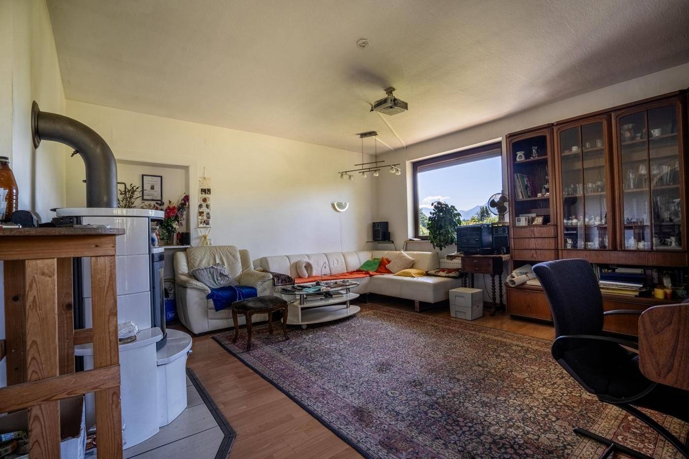 Geräumiges Wohnzimmer mit Kachelofen, Teppich und großem Fenster mit Bergblick.