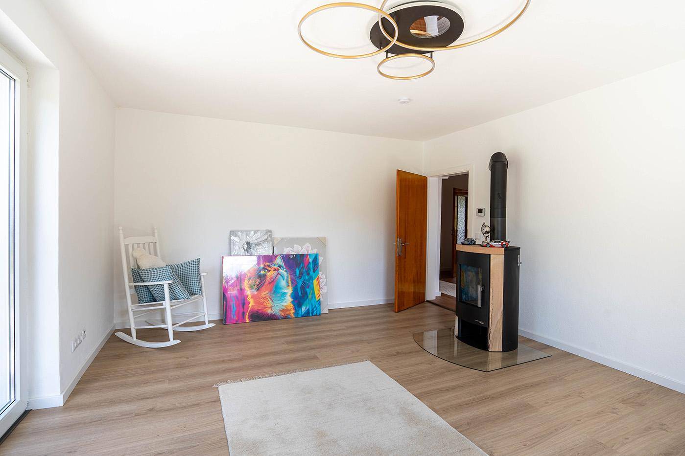 Helles Wohnzimmer mit modernem Holzofen, Laminatboden und weiß gestrichenen Wänden.