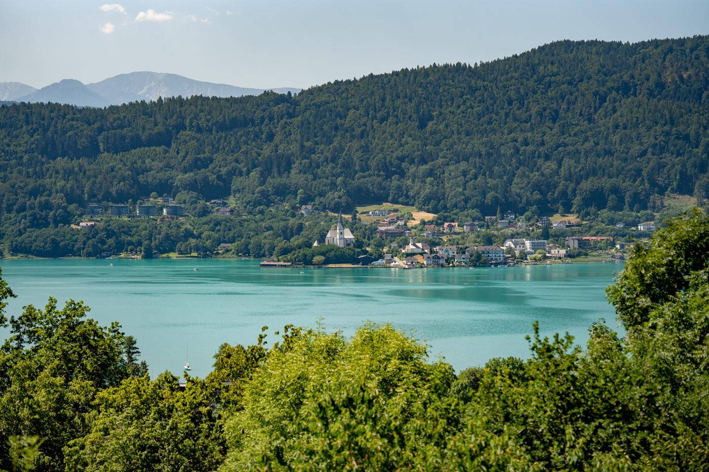 Weitläufiger Blick auf den See, bewaldete Hügel und ein malerisches Dorf am Ufer.