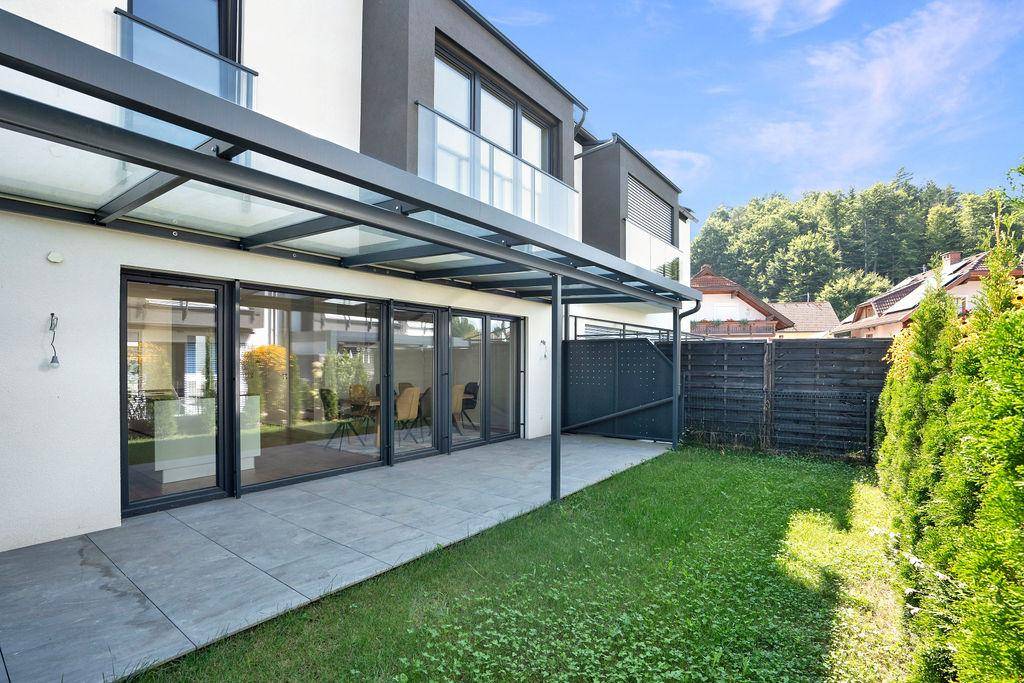 Überdachte Terrasse mit kleinem Rasenbereich und Blick auf die grüne Umgebung des Hauses.