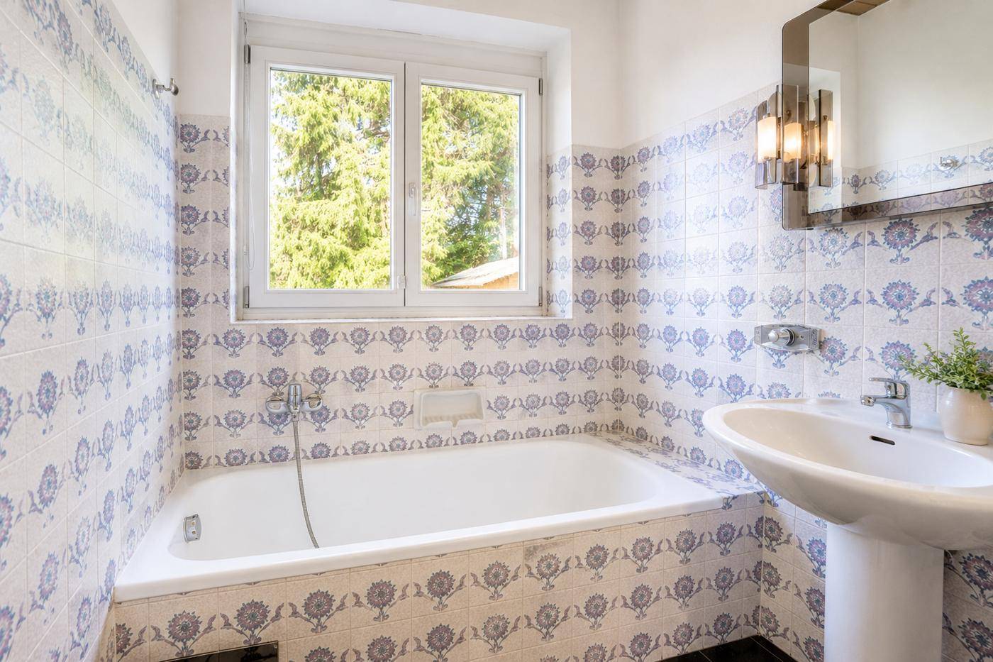 Badezimmer mit Badewanne, Waschbecken und auffälligen blau-weißen Fliesen, inklusive Fenster.