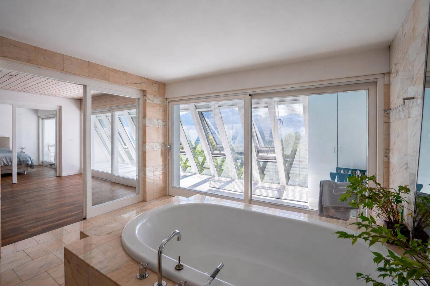 Modernes Badezimmer mit Badewanne, Fliesenboden und großen Fenstern mit Bergblick.