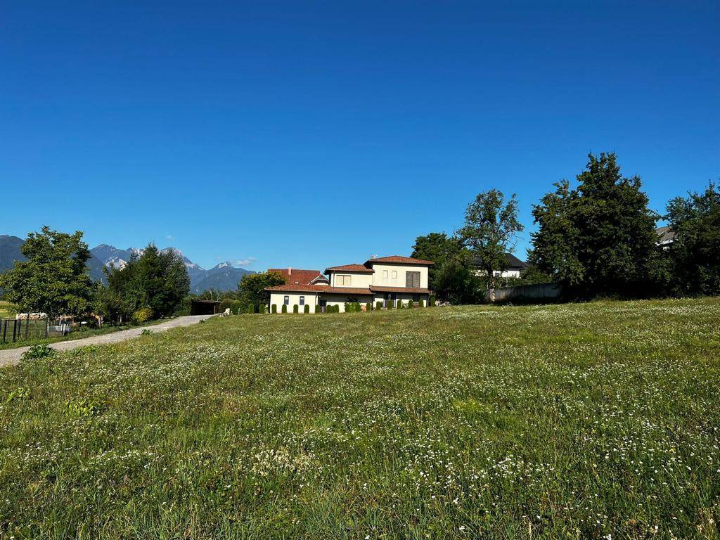 Modernes Haus mit Flachdach und Terrassen in einer weiten grünen Landschaft mit Bergsicht.