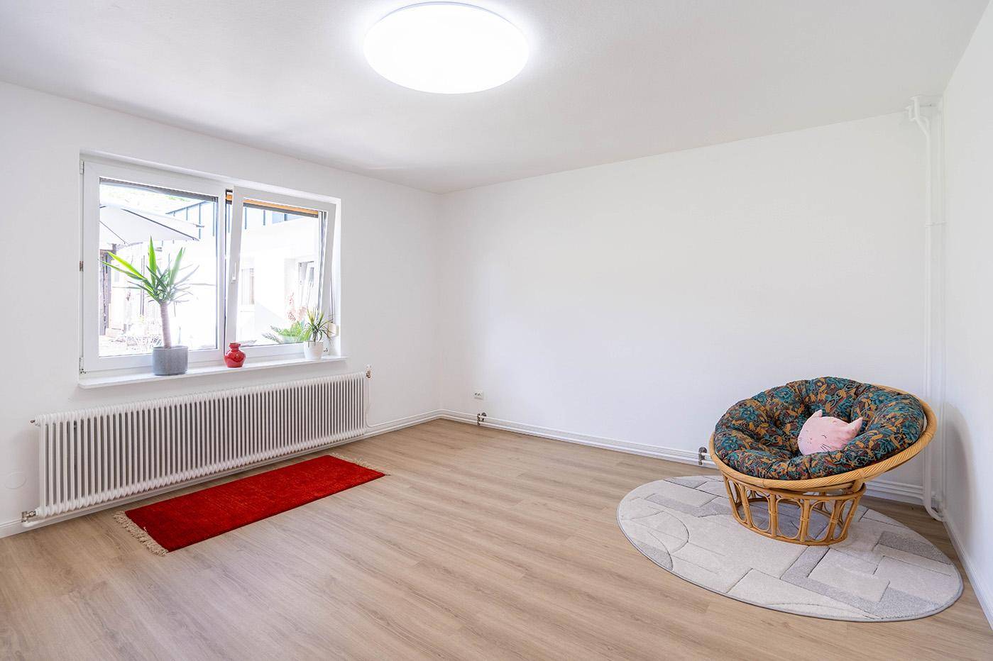 Freundlicher Raum mit Laminatboden, großem Fenster und einem bequemen Sessel.