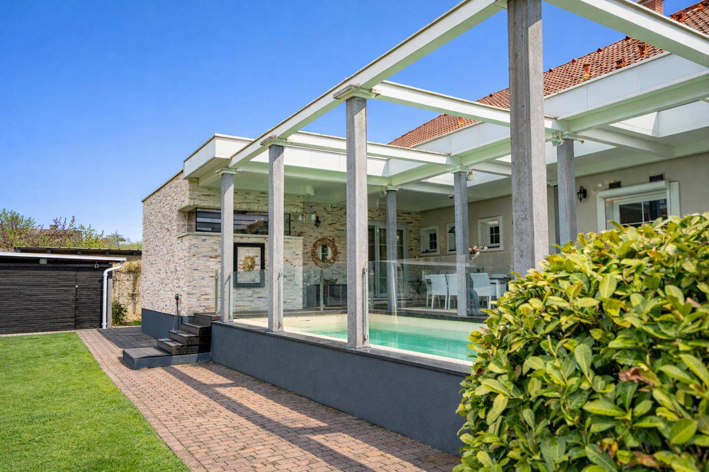 Überdachter Poolbereich mit Glaswänden und direktem Zugang zum Garten.