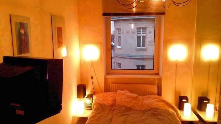 Schlafzimmer mit Bett, Nachttischen und warmem Licht, mit Blick auf die umliegenden Gebäude.