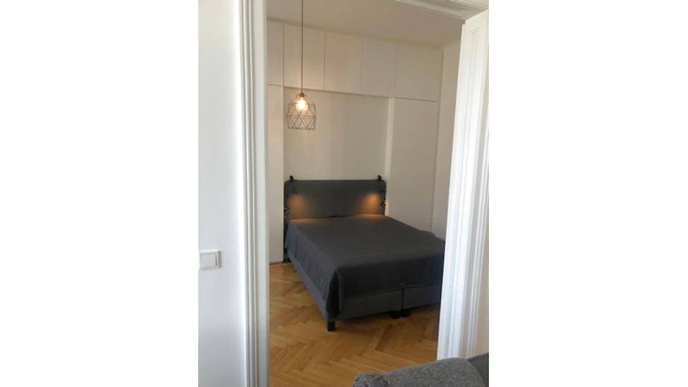 Schlafzimmer mit Doppelbett und Einbauschränken, gesehen durch einen Türrahmen, mit Parkettboden.