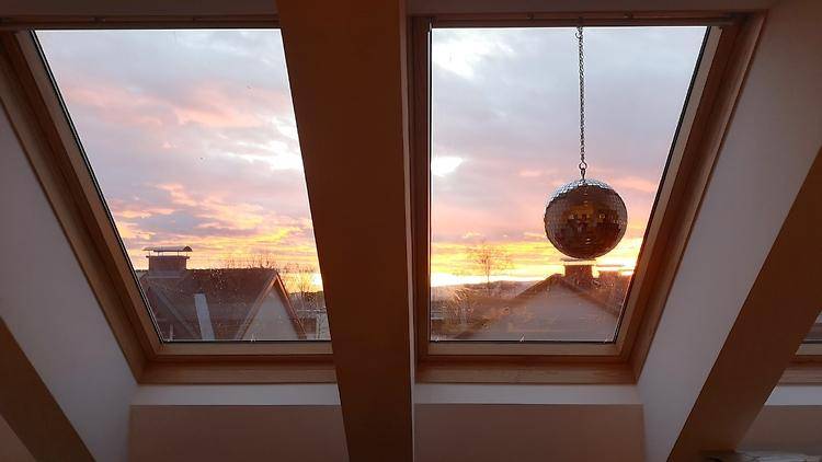 Sonnenuntergangsblick durch Dachfenster mit einem glitzernden Dekorationselement im Vordergrund.