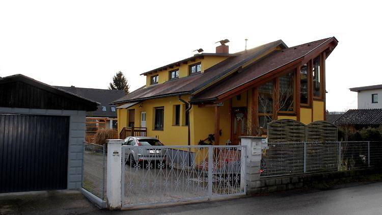 Gelbes Einfamilienhaus mit markantem Dach, Garage und Vorgartenbereich.