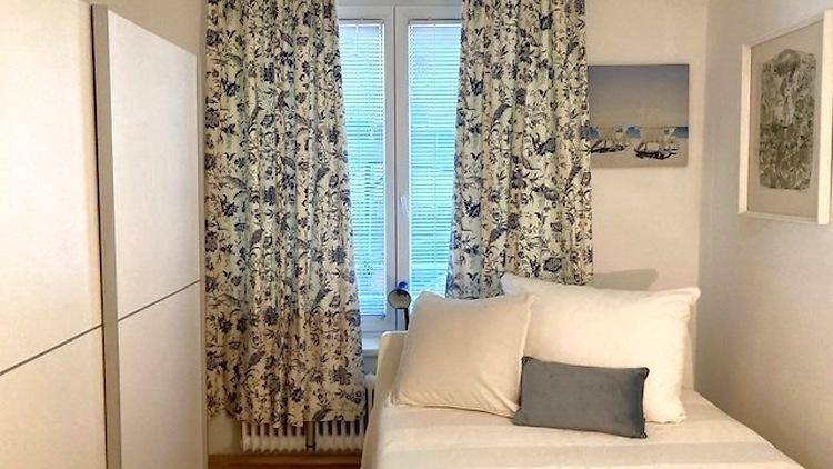Helles Schlafzimmer mit Einzelbett, floralen Vorhängen und Blick nach draußen.